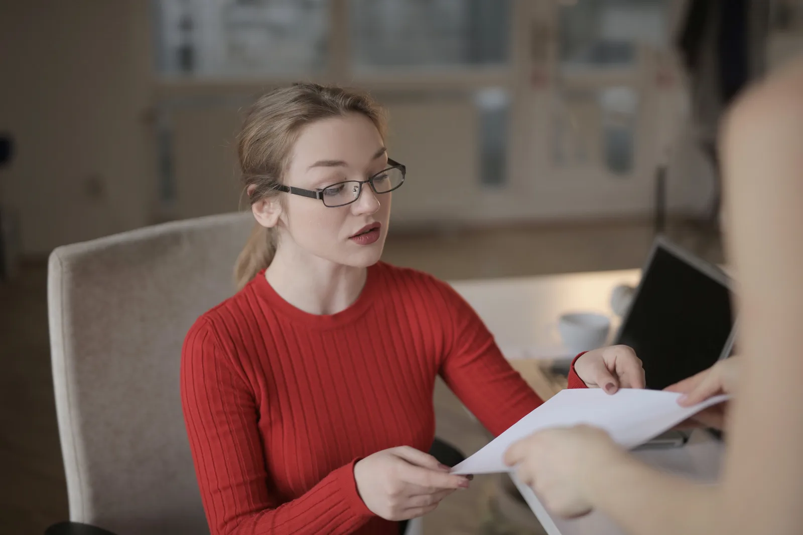 Caucasian woman in red sweater receiving document in a well-lit office setting.