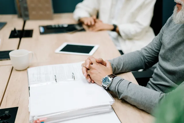 Close-up of a business meeting with documents and digital tablet on a wooden desk. Arbejdsmarkedets spilleregler: Rekruttering, ansættelse og afskedigelse i danske virksomheder