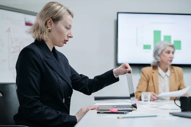 Two businesswomen discussing data in a modern office setting with laptop and charts. Bæredygtighedsrapportering: Krav, standarder og praktisk implementering i danske virksomheder